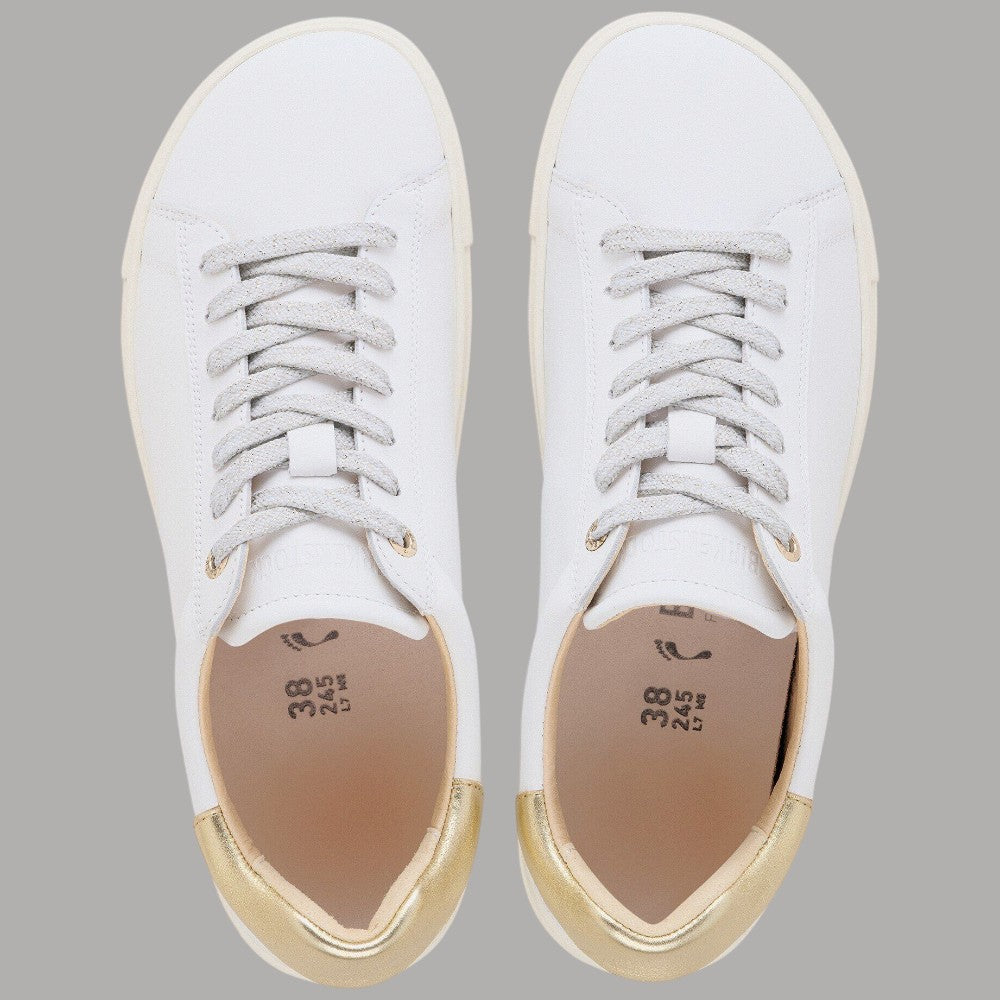 Paio di sneaker bianche aperte: etichetta interna marrone e bordo oro al colletto