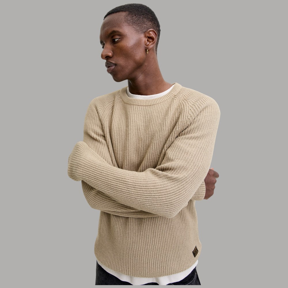 Maglione a coste beige chiaro con girocollo, braccia incrociate.
