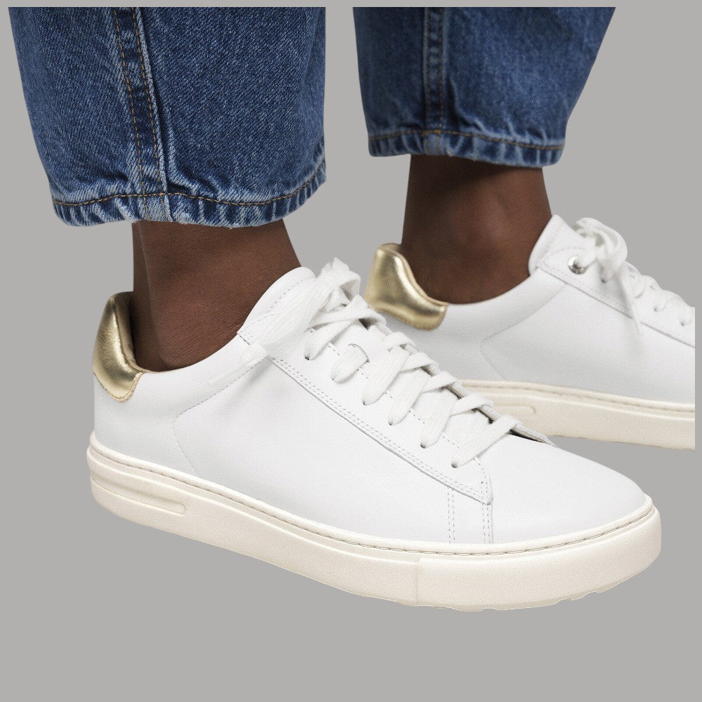 Sneaker bianche in pelle con lacci grigi e tallone oro indossate con jeans