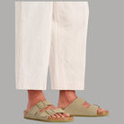 Ciabatte khaki con due cinturini indossate, con pantaloni bianchi sopra la caviglia