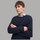 Maglione a coste blu scuro con girocollo, braccia incrociate.