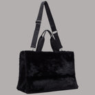 Borsa tote grande in pelliccia nera con patta centrale e tracolla regolabile.