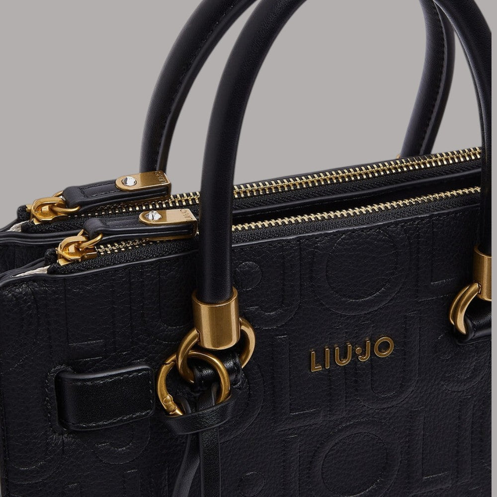 Dettaglio manici e zip borsa a mano piccola nera con logo a rilievo e finitura dorata.