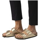 Ciabatte Birkenstock Arizona oro indossate, pantaloni neri e fibbie lucide