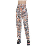 Pantaloni fantasia vita alta: fondo nero con stampa arancio e bianco, gamba affusolata.